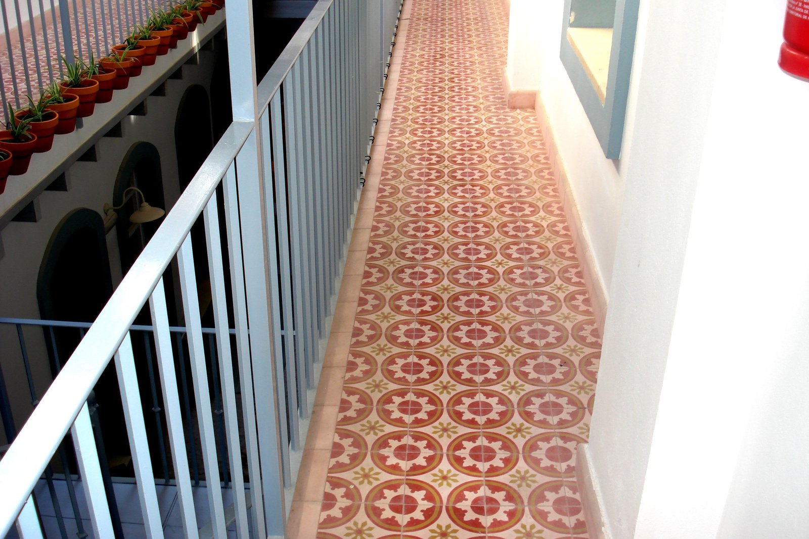 Corredor de hotel sobre un patio, pavimentado con baldosa hidráulica de dibujo circular en rojo, ocre y crema, con variación de tono entre piezas